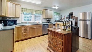 A kitchen with wooden cabinets, a stainless steel refrigerator, a dishwasher, and a central island with drawers. - Crackerbox Palace (Sylva)