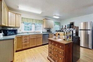 A kitchen with wooden cabinets, a stainless steel refrigerator, a dishwasher, and a central island with drawers. - Crackerbox Palace (Sylva)