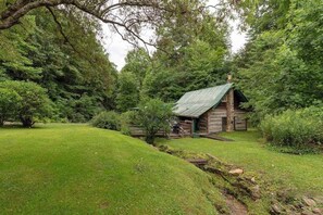 A rustic log cabin with a green roof, surrounded by lush greenery and a well-maintained lawn. - Crackerbox Palace (Sylva)