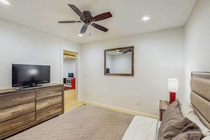 A bedroom with a bed, a TV, a dresser, a ceiling fan, a mirror, and a nightstand.