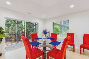 A dining area with a glass table, red chairs, and a vase with flowers.
