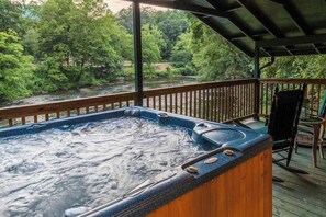 Ein Whirlpool auf einer Holzterrasse mit Blick auf einen Fluss und Bäume.