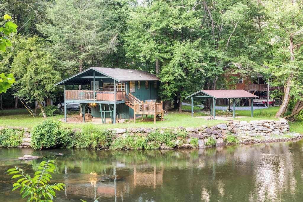 A cabin with a deck, a covered porch, and a pond in the foreground.