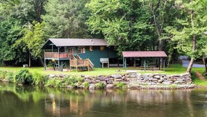 En stuga med en veranda, en överbyggd plats för picknick och en stenmur vid en sjö.