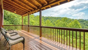 Eine Holzterrasse mit Geländer, zwei Korbstühle und Blick auf eine bewaldete Landschaft.