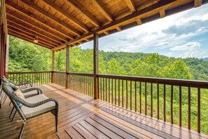 A wooden deck with a railing, two wicker chairs, and a view of a forested landscape. - Close to Heaven (Sylva)