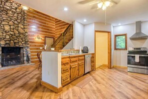 A kitchen with wooden cabinets, a stone wall, a fireplace, and a modern oven. - Close to Heaven (Sylva)