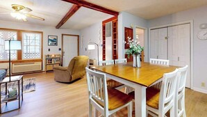 Un coin repas avec une table en bois et des chaises blanches, un canapé, une lampe et une bibliothèque.