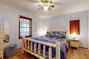 Ein Schlafzimmer mit einem hölzernen Bett, einem Deckenventilator, einem Fenster mit Jalousien, einem Nachttisch mit Lampe und einem wandmontierten Schrank.