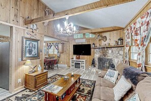 Un intérieur rustique avec des murs en bois, une cheminée en pierre, un téléviseur et un coin salon confortable.