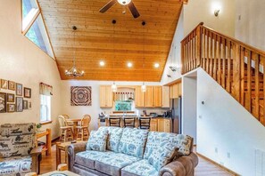 Ein geräumiges Wohnzimmer mit hoher Decke, einer Holztreppe und einem Küchenbereich mit Holzschränken und einem Esstisch.
