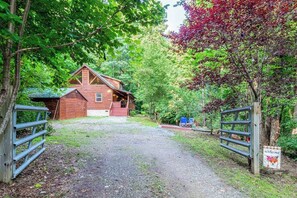 Eine rustikale Holzhütte mit Kiesweg, umgeben von üppigem Grün und einem Holztor.
