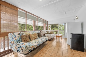Eine überdachte Terrasse mit einer Couch, einem kleinen Tisch und einem Kühlschrank.