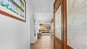 Un couloir doté d’un plancher en bois, des œuvres d’art encadrées accrochées aux murs et une vue sur une pièce comprenant un lit et une fenêtre.