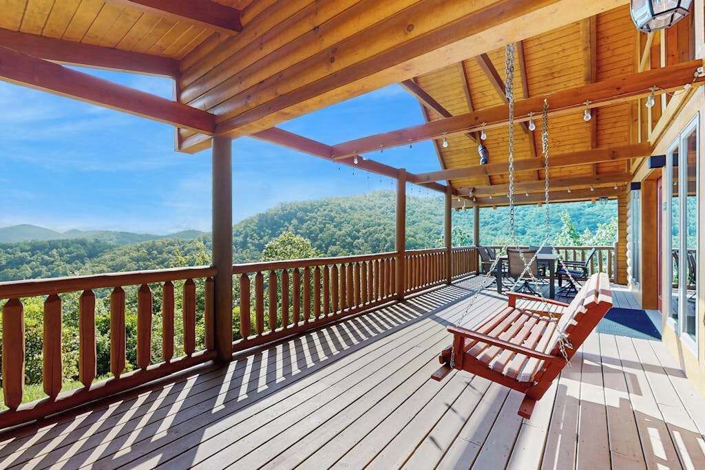 A wooden deck with a view of the mountains, a red bench, and a table with chairs.