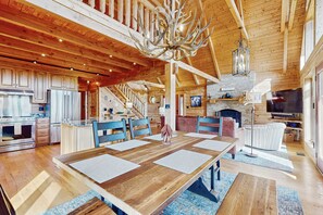 Ein großzügiges Blockhaus-Interieur mit einem großen Esstisch, einer Küche und einem Kamin.