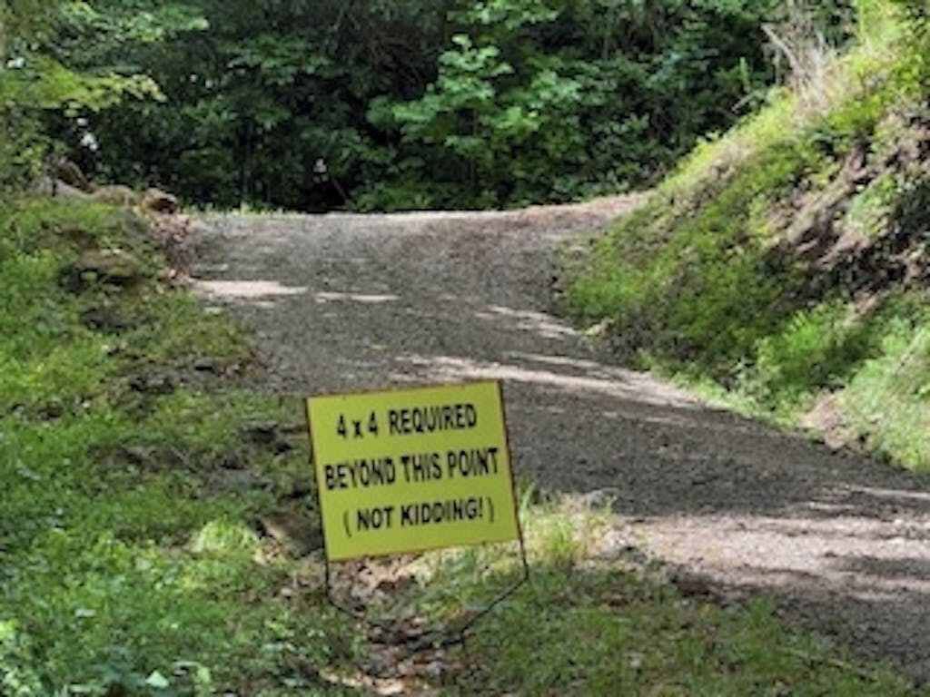 Een bord langs een onverharde weg in een bebost gebied.