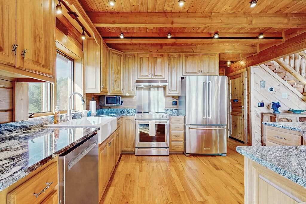 L’intérieur d’un chalet en bois comprend une cuisine dotée de plans de travail en granit, d’appareils électroménagers en acier inoxydable et d’un plafond en bois.