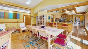 Una habitación amplia con una gran mesa de comedor, sillas, una estantería y una zona de cocina.