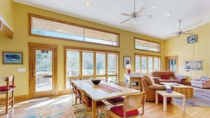 Un salón amplio con una gran mesa de comedor de madera, asientos cómodos y ventanas grandes que ofrecen vistas al exterior.