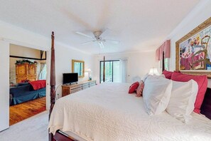 A bedroom with a large bed, a ceiling fan, a television, and a painting on the wall.