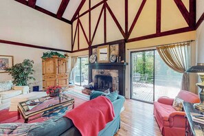 A spacious living room with a fireplace, wooden beams, and a large window.