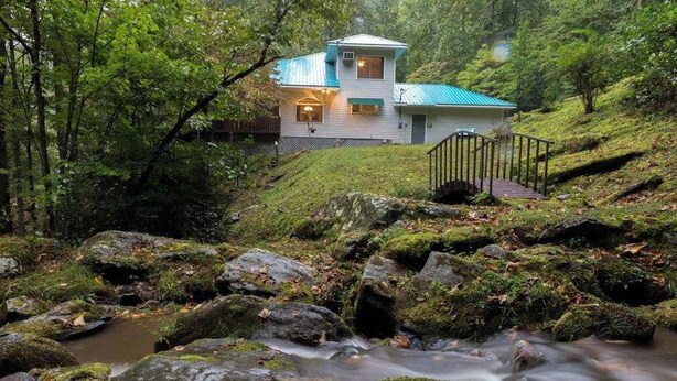 Una casa con tetto in metallo, una scala che conduce all'ingresso e un ruscello in primo piano.