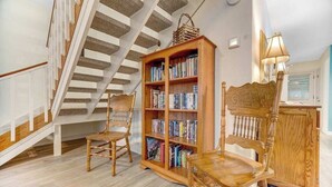 Una scala con ringhiere in legno, una libreria di legno piena di libri e due sedie di legno.