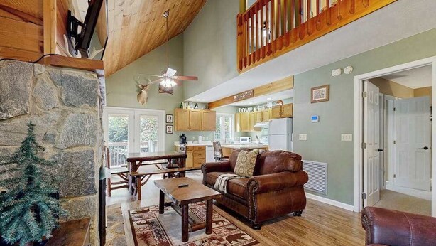 A spacious living room with a stone fireplace, a wooden ceiling, a leather sofa, and a view into the kitchen. - Smoky View Retreat (Maggie Valley)