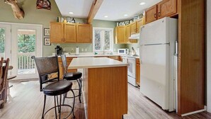 A kitchen with wooden cabinets, a white refrigerator, and a deer head mounted on the wall. - Smoky View Retreat (Maggie Valley)