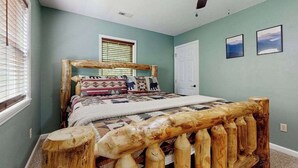 A bedroom with a wooden bed frame, a ceiling fan, a window with blinds, and a door. - Smoky View Retreat (Maggie Valley)