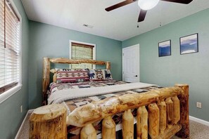 Ein Schlafzimmer mit einem hölzernen Bettgestell, einem Deckenventilator, einem Fenster mit Jalousien und einer Tür.