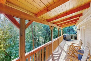 Eine Holzterrasse mit Geländer, Holzstühlen und Blick auf einen Wald.