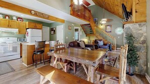 A rustic interior with a wooden dining table, kitchen area, and a staircase leading to another level. - Smoky View Retreat (Maggie Valley)