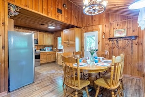 A wooden cabin interior with a dining table, chairs, a refrigerator, wooden cabinets, and a ceiling fan. - Rustic & wooded wonder w/ hot tub, wraparound deck, firepit, & fast WiFi (Whittier)