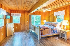 A wooden cabin bedroom with a bed, bedside table, and a television on the wall. - Rustic & wooded wonder w/ hot tub, wraparound deck, firepit, & fast WiFi (Whittier)