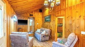 A wooden interior with a sofa, two armchairs, a TV, and a chandelier. - The Outpost (Whittier)