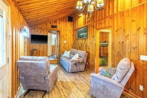 A wooden interior with a sofa, two armchairs, a TV, and a chandelier. - Rustic & wooded wonder w/ hot tub, wraparound deck, firepit, & fast WiFi (Whittier)