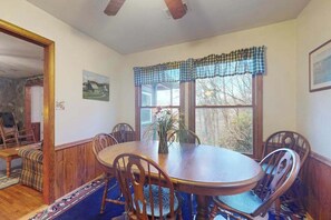 Ein Esszimmer mit einem Holztisch und Stühlen, einem Fenster mit karierter Vorhangschlaufe und einem Bild an der Wand.