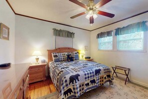 Ein Schlafzimmer mit einem Bett, Nachttischen, einer Holzkommode, einem Deckenventilator und einem Fenster mit Vorhängen.