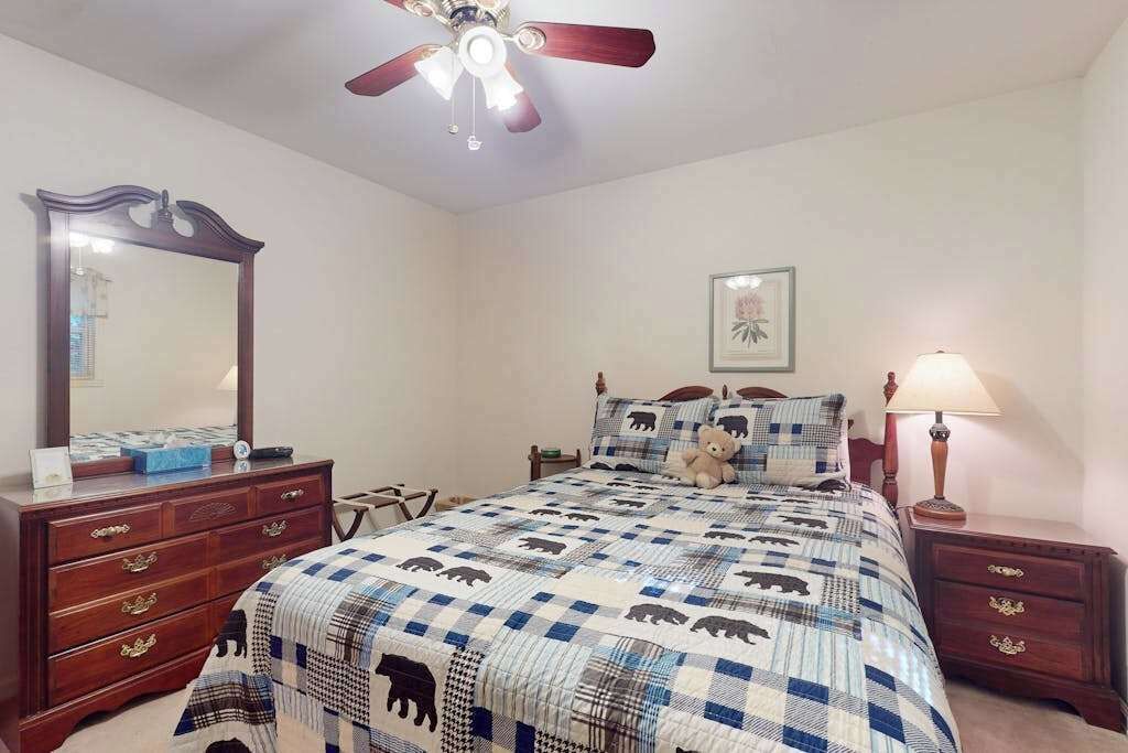 A bedroom with a bed, a dresser, a nightstand, a ceiling fan, and a framed picture on the wall.