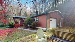 Eine rustikale Holzhütte mit überdachter Veranda, einer Holzbank und einem Sessel in einem bewaldeten Gebiet.