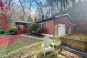 Eine rustikale Holzhütte mit überdachter Veranda, einer Holzbank und einem Sessel in einem bewaldeten Gebiet.