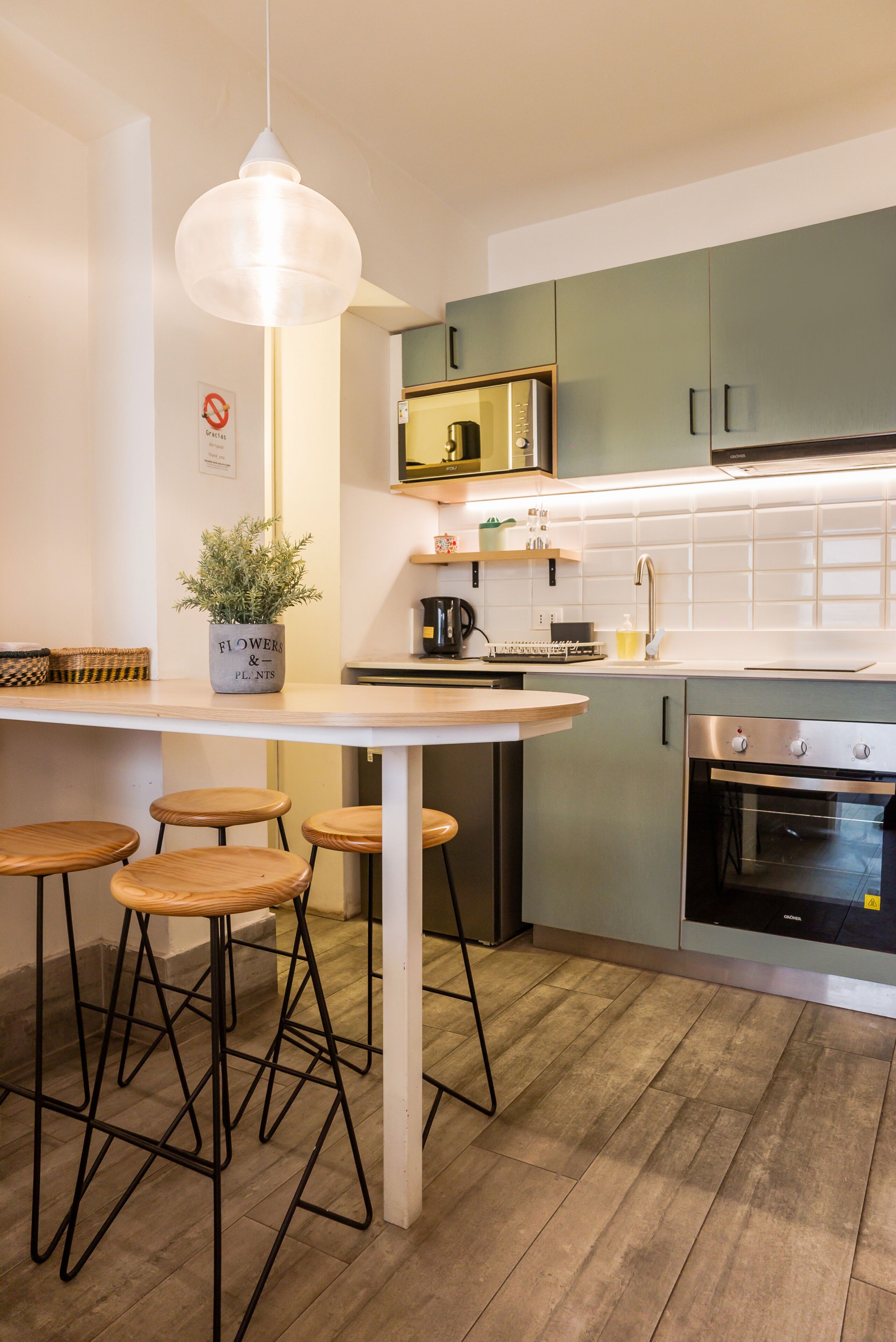 Una cocina moderna con una isla blanca, taburetes de bar, una lámpara colgante y un horno empotrado.