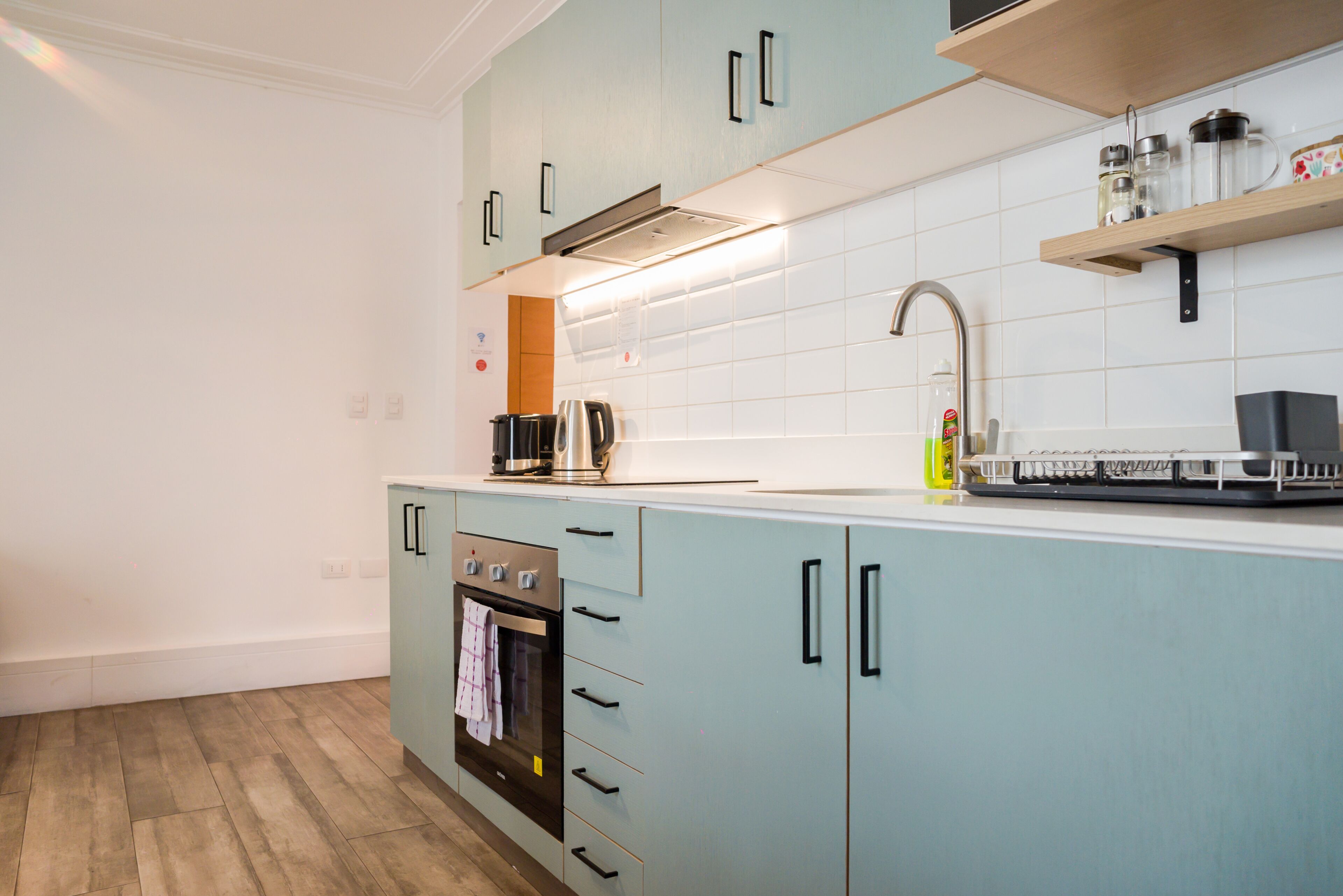 A kitchen with a built-in oven, a stainless steel kettle, and a coffee maker on the countertop.