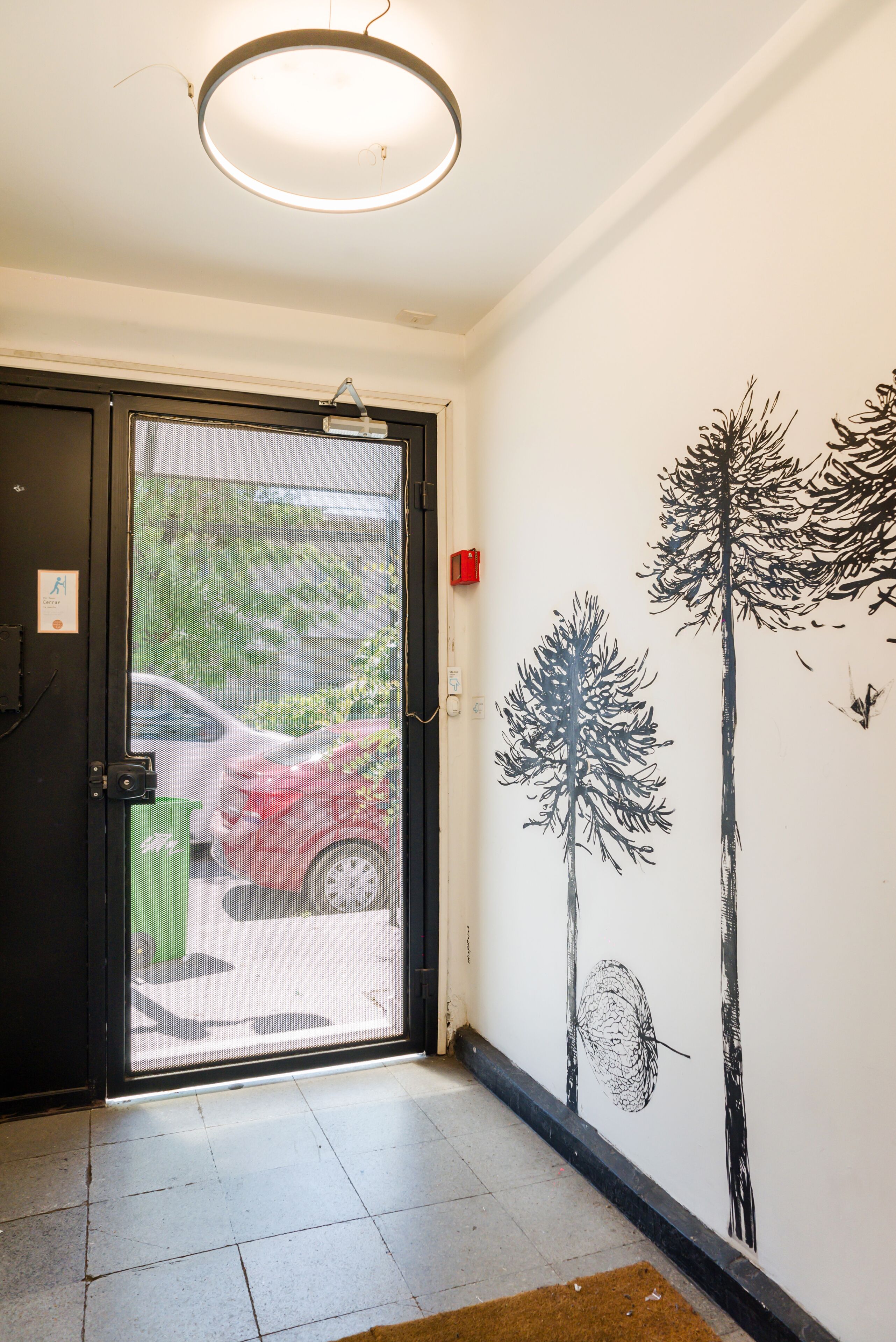 Une porte avec un moustiquaire, un mur décoré de peintures murales représentant des arbres et un luminaire au plafond.