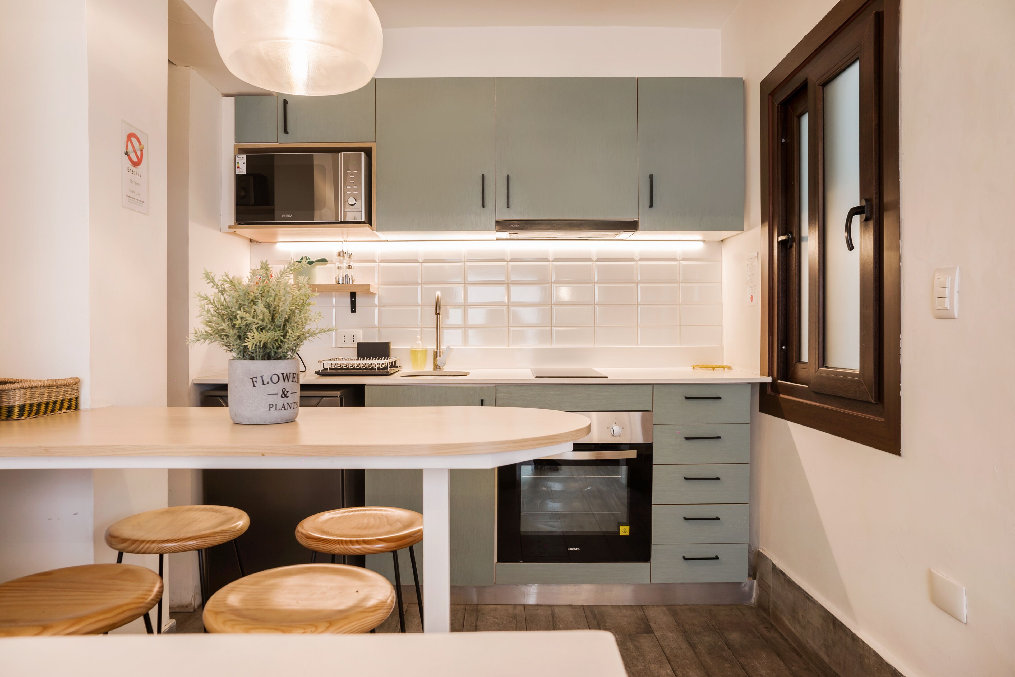 A modern kitchen with a central island, bar stools, a microwave, oven, and a potted plant.