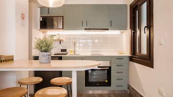 Cocina moderna con una isla central, taburetes de bar, microondas, horno y una planta en maceta.