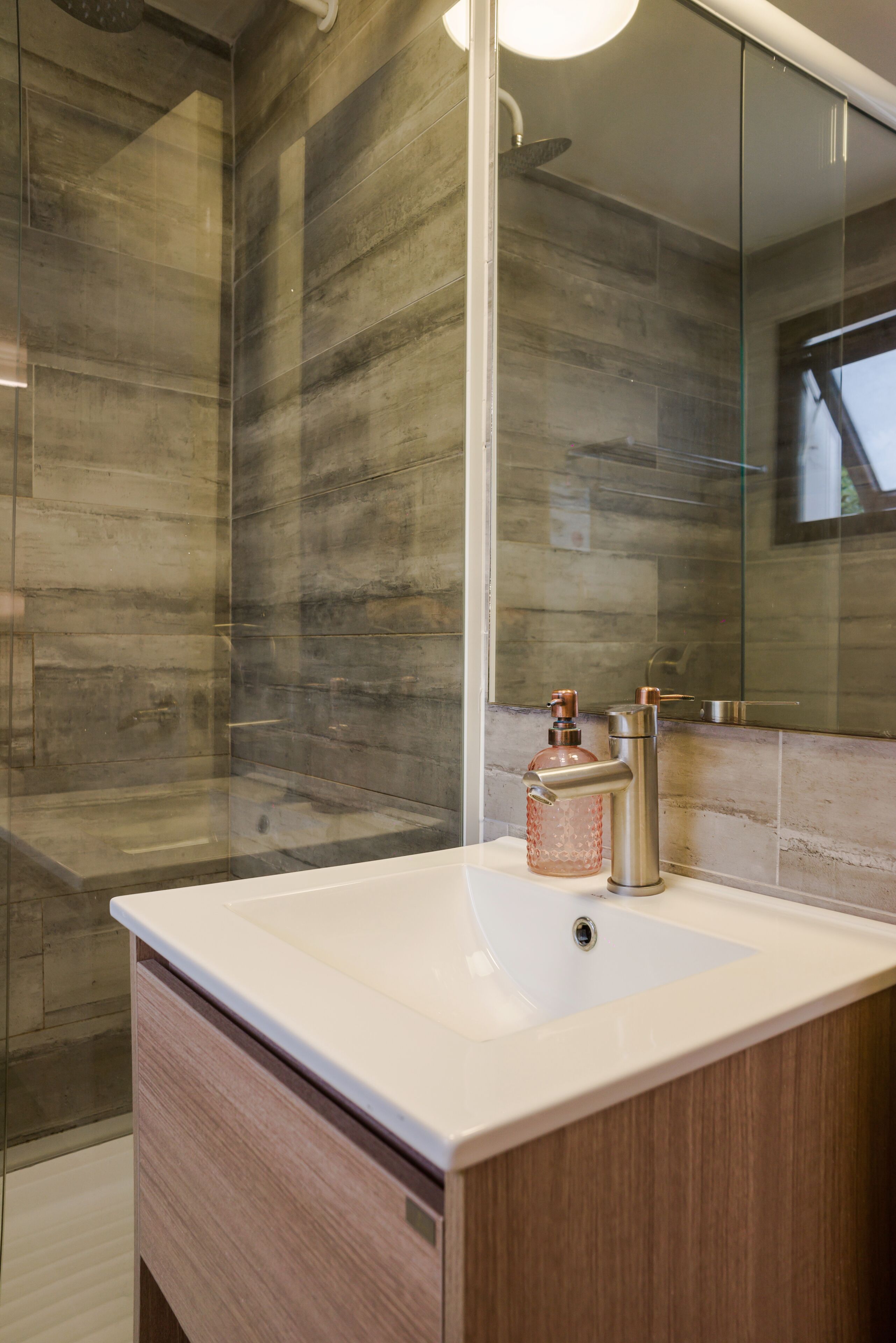 A modern bathroom with a glass shower enclosure, a white sink with a wooden vanity, and a large mirror.