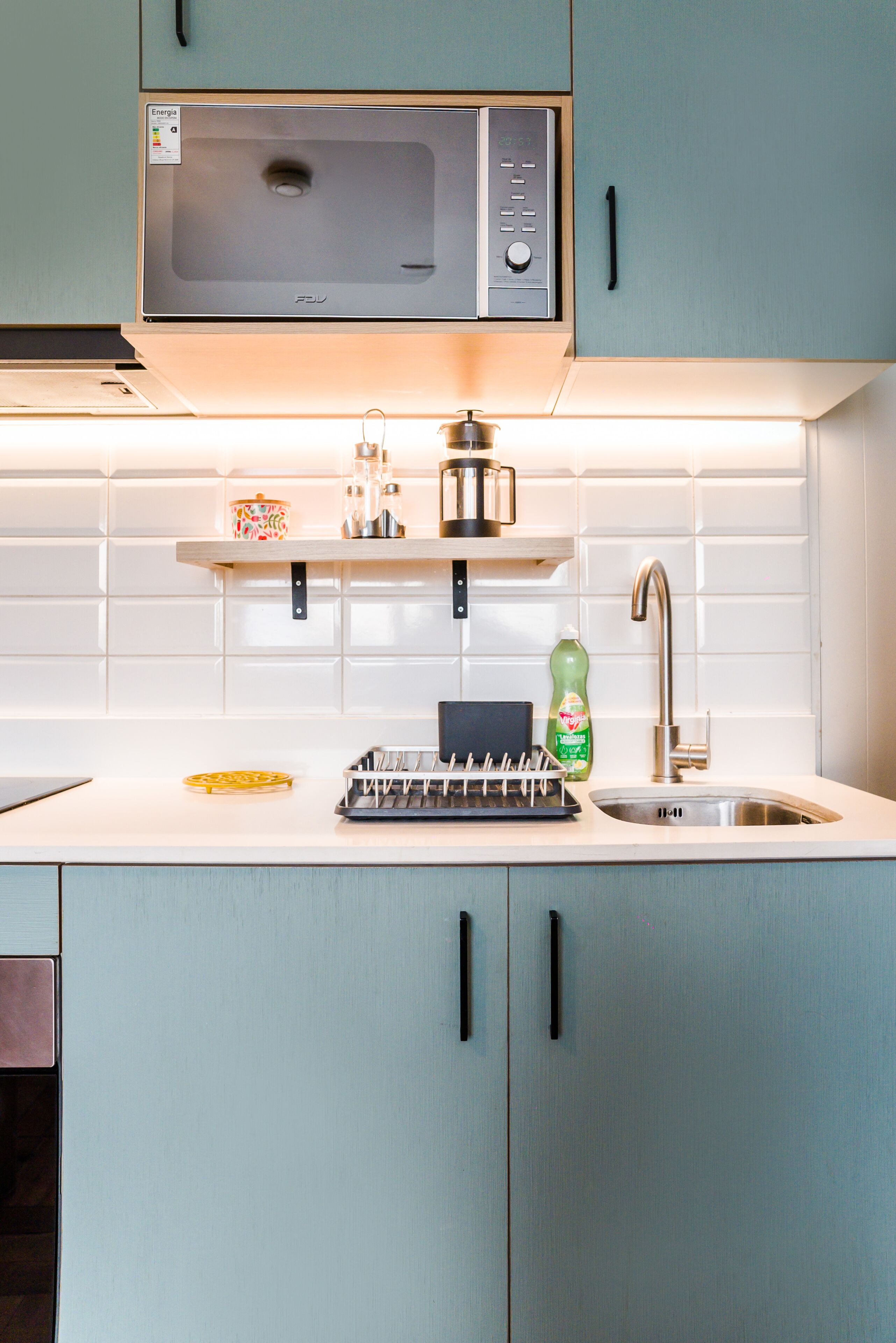 Una cocina con microondas, lavamanos y armarios.
